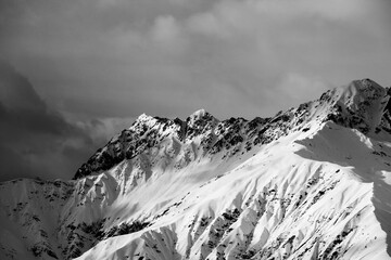 Black and white high snowy sunlight mountain and cloudy grey sky at winter evening