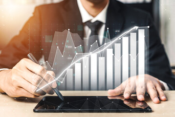 A business professional engages in data analysis using a digital tablet, with visual financial graphs depicting growth trends in a modern office, illustrating strategic insights. Impute