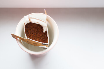 Drip bag in a ceramic cup on windowsill. Instant freshly brewed alternative filter drink in mug. Easy brew black coffee method for home, travel or office. cozy trendy lifestyle