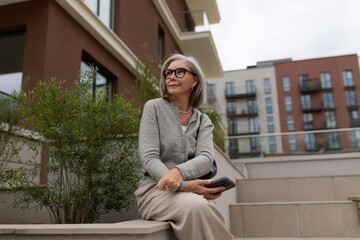Elegant woman sitting on a modern step in a city setting enjoying a peaceful moment with her phone