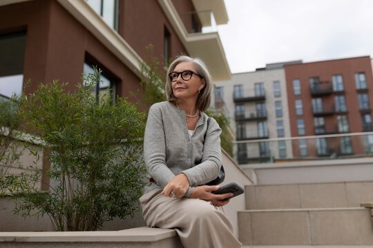Elegant woman sitting on a modern step in a city setting enjoying a peaceful moment with her phone
