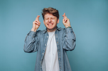 Young man with fingers crossed, eyes closed, hoping for luck.
