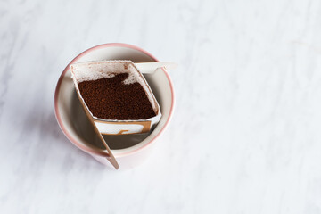 Drip bag in a ceramic cup on windowsill. Instant freshly brewed alternative filter drink in mug. Easy brew black coffee method for home, travel or office. cozy trendy lifestyle