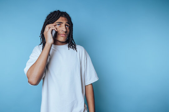 Young man with dreadlocks talking on a smartphone against a blue background.