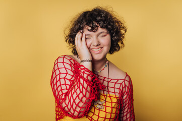Smiling person with curly hair in red netted top against yellow background. © bodnarphoto
