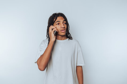 Young man with dreadlocks talking on a smartphone against a plain background.