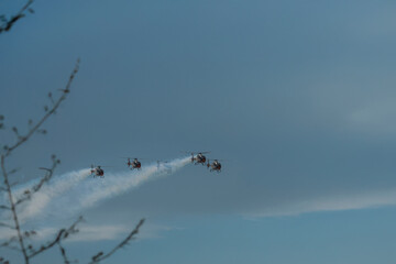 Helicopter squadron approaching with blue smoke trails in sky.