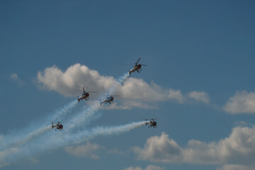 Five helicopters crossing paths during aerobatic smoke display.