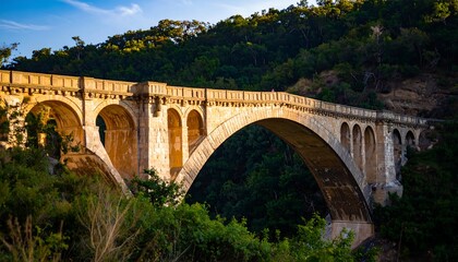 A majestic stone arch bridge spans a valley, bathed in golden sunlight, showcasing ancient architecture against a backdrop of lush green hills.