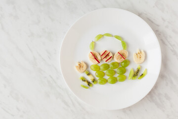 Creative healthy snack of breakfast for kids fruit bunny shaped on white plate, easter eggs around. Rabbit, basket makes from grape, orange, banana, apple. Top view