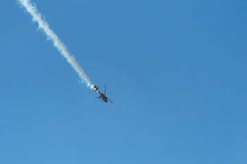 Helicopter diving with smoke trail against clear blue sky.