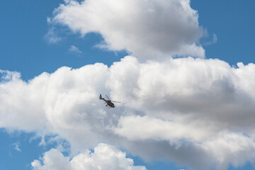 Training helicopter flying in front of large white clouds.