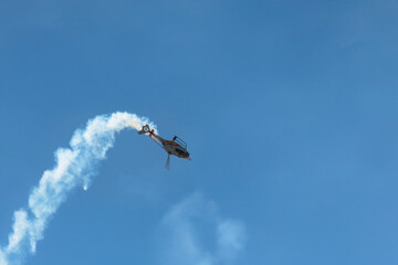 Aerobatic helicopter flying upside down with smoke trail.