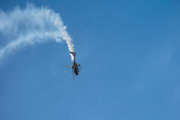 Helicopter performing spiral descent with smoke in clear sky.
