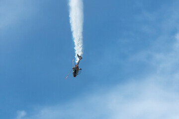 Aerobatic helicopter diving vertically with white smoke trail.