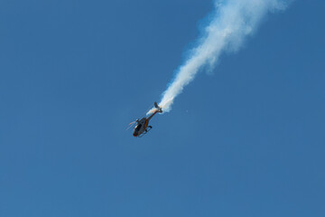 Single helicopter performing aerobatic maneuver with blue smoke.