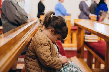 30.01.25 Vinnitsa, Ukraine: A little girl sits on a bench in a church during a service, spinning...