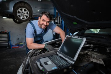 Car mechanic using a computer to diagnose a car engine problem
