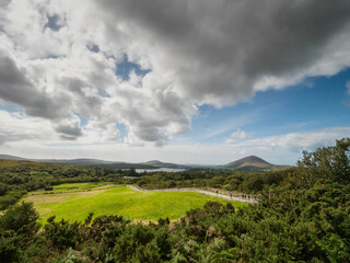 A lush green field with a mountain and ocean in the background. The sky is clear and blue. Beautiful nature view from Diamond hill, Connemara National Park, Ireland. Travel and tourism.