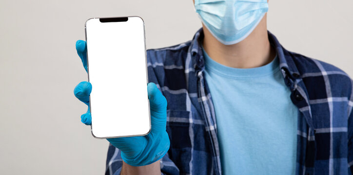Unrecognizable young man in face mask showing cellphone with covid-19 health passport on light studio background. Closeup of millennial guy showing coronavirus immunization certificate