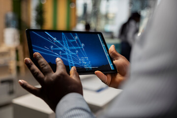 Fototapeta na wymiar Close up of engineer working for green tech company designing eco power line towers on tablet. RD specialist uses CAD app on device to optimize transmission tower systems, reducing carbon footprint