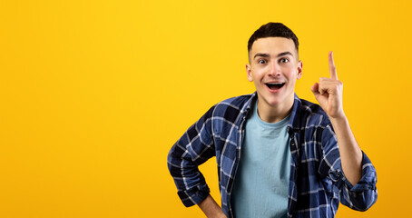 Handsome young guy in casual clothes pointing upwards on orange studio background. Millennial man...