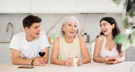 Cheerful elderly mother having good time with adult children drinking tea in live room