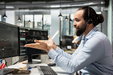 Stockbroker executing buy and sell orders for clients in stock market while talking with them in...