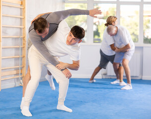 Fototapeta premium Man with sparring partner in gym during self-defense training, sparring and practicing technique of hip flip