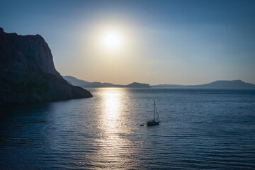 Yacht on the sea at sunset with rocky cliffs