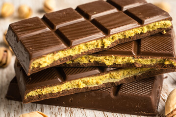 Close-up of stacked chocolate bars with pistachio filling on a rustic wooden surface background, known as Dubai chocolate. Ideal for dessert, sweets, gourmet food, and confectionery themes.