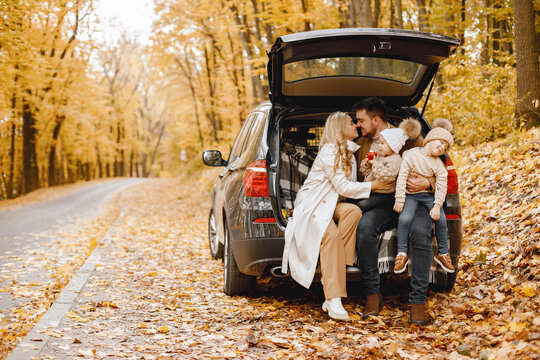 Young family sitting at open trunk of hatchback car in autumn forest