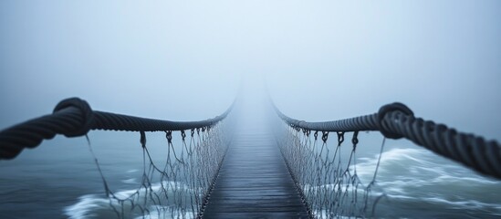 Fototapeta premium Mystical Suspension Bridge Disappearing into Thick Fog Over Troubled Waters