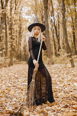 Young witch in forest on Halloween with a broom