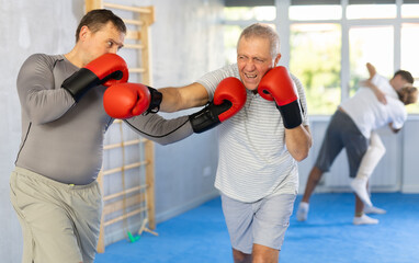 Male co-participant and senior man sparring partners during training battle fight using technique of boxing match. Boxing section for men, sport as lifestyle