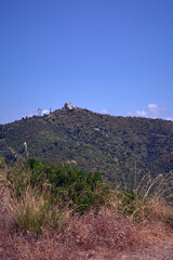 The Hermitage of Sant Ramon stands on the top of a dry hill under a clear blue sky. The photo captures the beauty and tranquility of the natural and rural landscape in Catalonia.