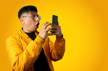Surprised latin man reacting to a smartphone notification isolated on yellow background, awe...