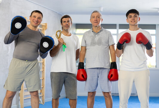 Four men of different ages in gym at group training session looking straight with sports equipment