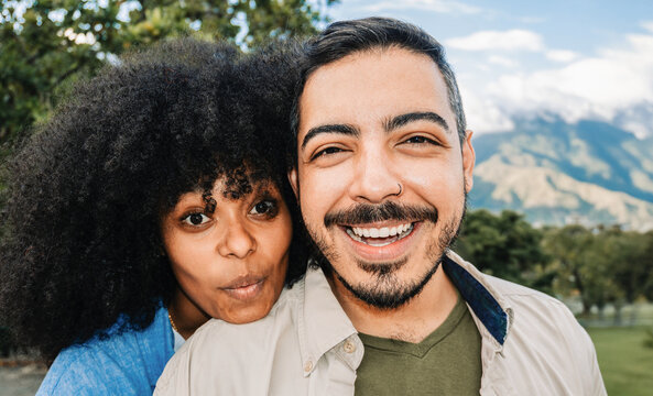 Young multiracial couple taking selfie in city park during travel vacation - Focus on afro latina girl face - Powered by Adobe
