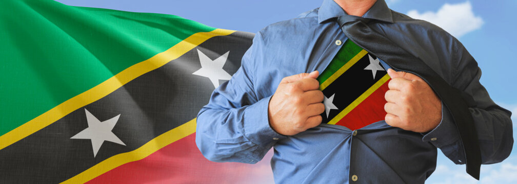 A businessman opening his shirt like super hero with Saint Kitts and Nevis flag and shows how patriotic he is by revealing his countries flag beneath printed on a t-shirt.