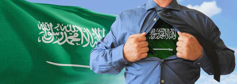 A businessman opening his shirt like super hero with Saudi Arabia flag and shows how patriotic he is by revealing his countries flag beneath printed on a t-shirt.