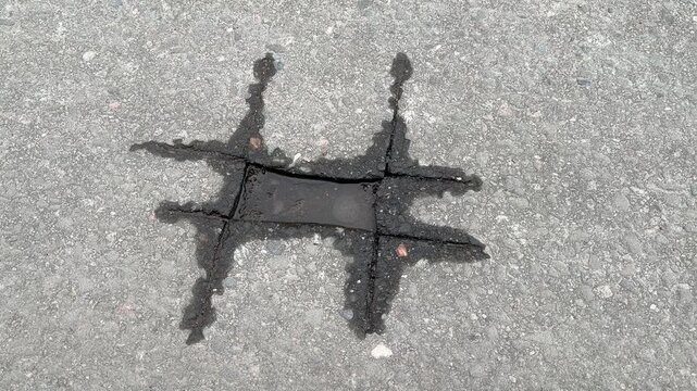 This is a Unique and Distinctive Asphalt Crack Pattern Found on the Road Surface. A particularly striking and unusual asphalt crack that closely resembles a hashtag pattern found on a road surface.
