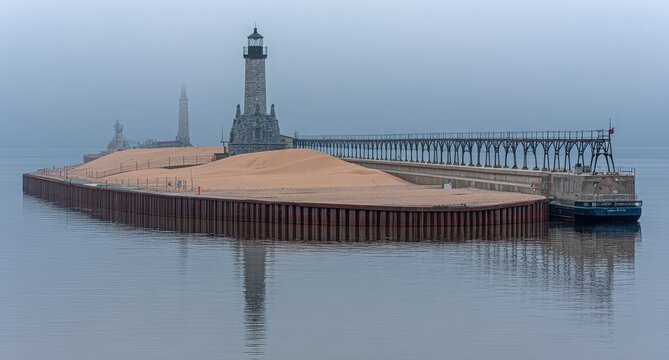 Misty morning at a sandy harbor, lighthouse and pier reflected - Powered by Adobe