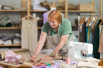 Dressmaker woman works in a sewing workshop and creates patterns of clothes on paper. Tailor with a measuring tape creates a fashion design