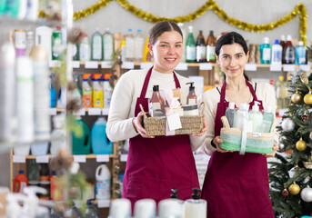 Girls sellers i presents bath cosmetic set, advertises organic cosmetic products in store. Employee with product in hands is waiting for customers in store hall. .
