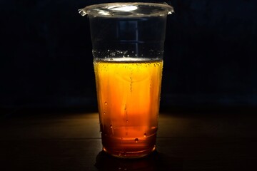 Plastic cup filled with iced tea and condensation droplets, illuminated dramatically against a dark background