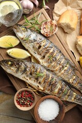 Tasty roasted seabass fish served with bread, rosemary and lemon on wooden table, flat lay. Homemade seafood dish