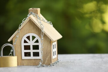 Home security. House model, chain and padlock on light grey table outdoors, closeup. Space for text
