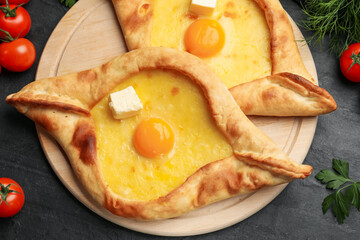 Tasty khachapuri with cheese, egg and other products on black table, flat lay