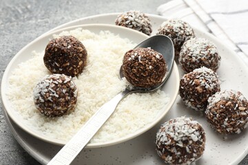 Making tasty chocolate candies with coconut flakes at grey table, closeup
